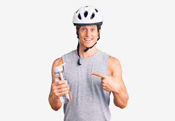 Young handsome man wearing bike helmet holding bottle of water smiling happy pointing with hand and finger