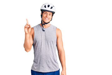 Young handsome man wearing bike helmet showing and pointing up with finger number one while smiling confident and happy.