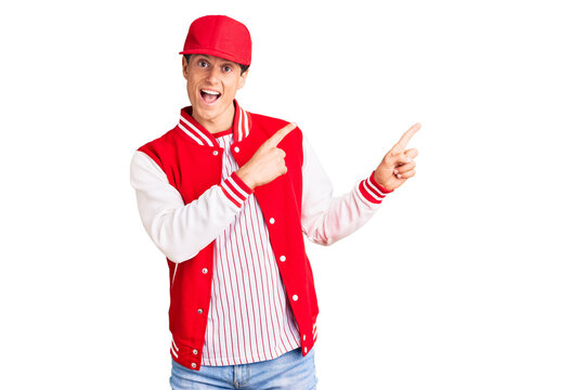 Young handsome man wearing baseball uniform smiling and looking at the camera pointing with two hands and fingers to the side.