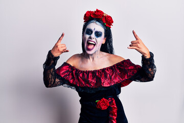 Young woman wearing mexican day of the dead makeup shouting with crazy expression doing rock symbol...