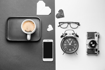 Composition with cup of coffee, photo camera, alarm clock and mobile phone on white and black background