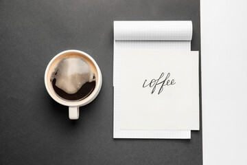 Cup of coffee with notebook on dark background