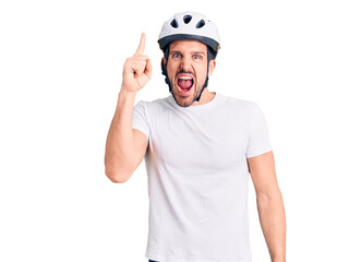 Young handsome man wearing bike helmet pointing finger up with successful idea. exited and happy. number one.