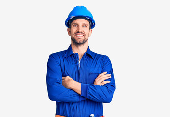 Young handsome man wearing worker uniform and hardhat happy face smiling with crossed arms looking at the camera. positive person.