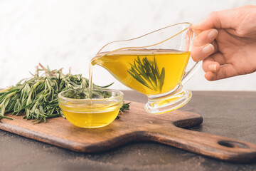 Woman pouring rosemary oil from gravy boat into bowl on table