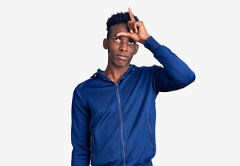 Fototapeta premium Young african american man wearing sportswear making fun of people with fingers on forehead doing loser gesture mocking and insulting.