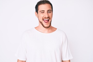 Young handsome man wearing casual white tshirt winking looking at the camera with sexy expression, cheerful and happy face.