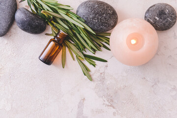 Fototapeta na wymiar Bottle of rosemary essential oil, aroma candle and spa stones on light background