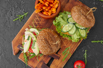 Board with tasty vegan burgers on dark background