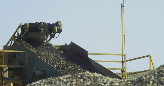 Stone crusher plant machine in the work process , transportation, and separation of gravel pebbles on the conveyor belt, rocks on vibrating hopper feeder the blue sky in the background, close-up shot.