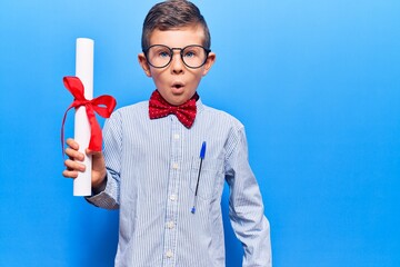 Cute blond kid wearing nerd bow tie and glasses holding diploma scared and amazed with open mouth...