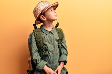Cute blond kid wearing explorer hat and backpack looking to side, relax profile pose with natural face and confident smile. - obrazy, fototapety, plakaty