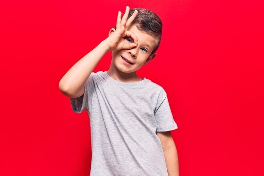 Cute blond kid wearing casual clothes smiling happy doing ok sign with hand on eye looking through fingers