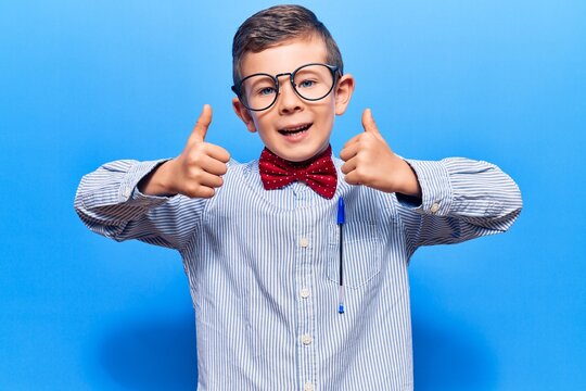 Cute blond kid wearing nerd bow tie and glasses success sign doing positive gesture with hand, thumbs up smiling and happy. cheerful expression and winner gesture.
