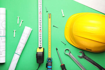 Measuring tapes with builder's supplies and blueprints on color background