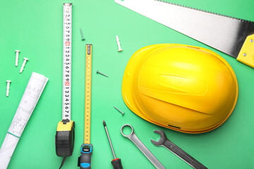 Measuring tapes with builder's supplies and blueprint on color background