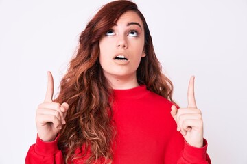 Young beautiful woman wearing casual clothes amazed and surprised looking up and pointing with fingers and raised arms.