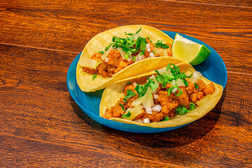 A couple of Pastor Tacos with cilantro, onion and lime on a wooden background