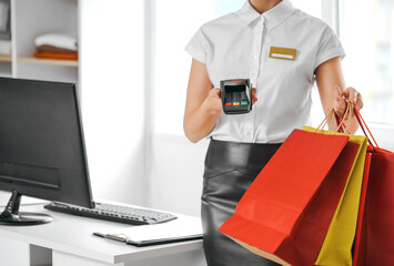 Female seller with shopping bags and payment terminal in modern clothes store