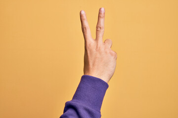 Hand of caucasian young man showing fingers over isolated yellow background counting number 2 showing two fingers, gesturing victory and winner symbol