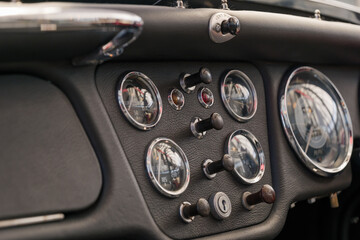 Selective focus, interior view of classic and vintage detail of gauge, switches, button, meter and steering wheel on black leather control panel dashboard inside old antique convertible car.