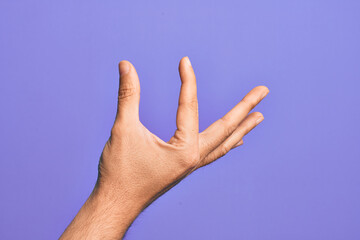 Hand of caucasian young man showing fingers over isolated purple background picking and taking invisible thing, holding object with fingers showing space