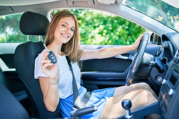 Young beautiful blonde woman smiling happy sitting at the car showing key