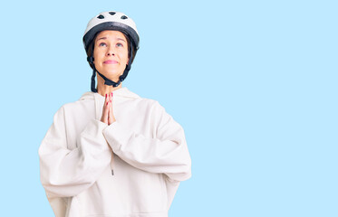 Beautiful brunette young woman wearing bike helmet and sporty clothes begging and praying with hands together with hope expression on face very emotional and worried. begging.