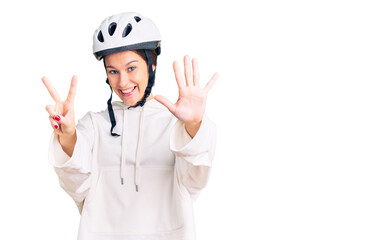 Beautiful brunette young woman wearing bike helmet and sporty clothes showing and pointing up with fingers number seven while smiling confident and happy.