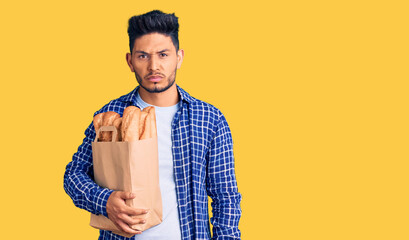 Handsome latin american young man holding paper bag with bread skeptic and nervous, frowning upset because of problem. negative person.