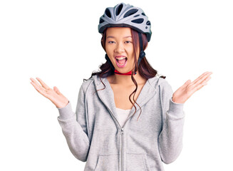 Young beautiful chinese girl wearing bike helmet celebrating victory with happy smile and winner expression with raised hands