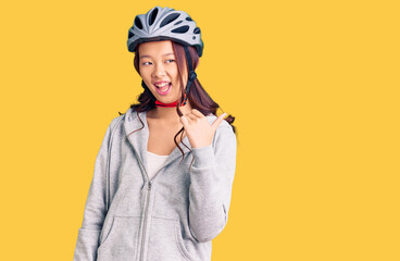 Young beautiful chinese girl wearing bike helmet smiling with happy face looking and pointing to the side with thumb up.