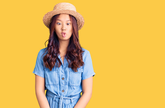 Young beautiful chinese girl wearing summer hat making fish face with lips, crazy and comical gesture. funny expression.