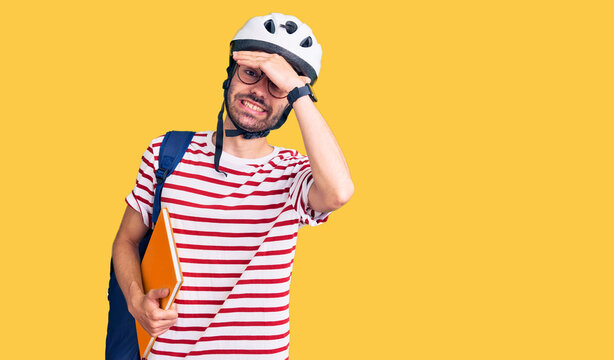 Young hispanic man wearing student backpack and bike helmet holding binder stressed and frustrated with hand on head, surprised and angry face