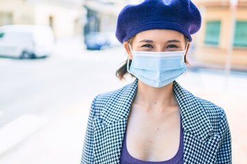 Young beautiful girl smiling happy wearing beret and medical mask walking at street of city