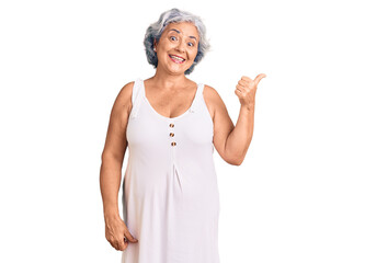 Senior woman with gray hair wearing casual clothes smiling with happy face looking and pointing to the side with thumb up.