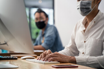 Asian young businessman wearing mask working on computer in office.	
