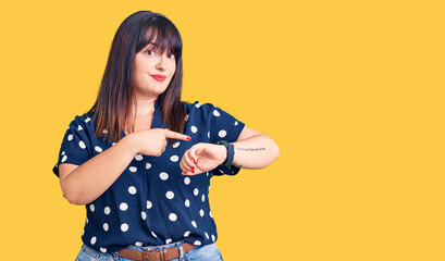 Young plus size woman wearing casual clothes in hurry pointing to watch time, impatience, upset and angry for deadline delay