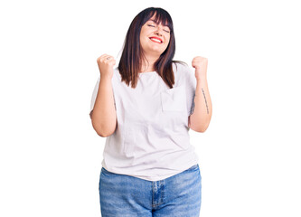 Obraz na płótnie Canvas Young plus size woman wearing casual clothes very happy and excited doing winner gesture with arms raised, smiling and screaming for success. celebration concept.