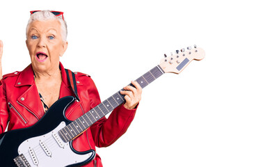 Senior beautiful woman with blue eyes and grey hair wearing a modern look playing electric guitar smiling with happy face winking at the camera doing victory sign with fingers. number two.