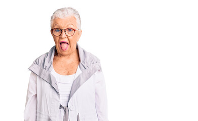 Senior beautiful woman with blue eyes and grey hair wearing casual clothes and glasses sticking tongue out happy with funny expression. emotion concept.