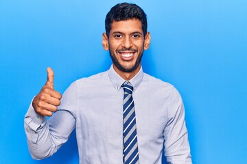 Young latin man wearing business clothes smiling happy and positive, thumb up doing excellent and approval sign