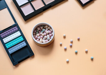 Makeup background. Eye shadow palette, powder, brushes, lipstick on yellow background. Flat lay, top view with copy space. Fashion, beauty, makeup, cosmetics.