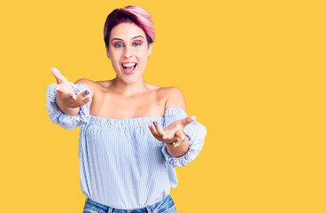 Young beautiful woman with pink hair wearing casual clothes smiling cheerful offering hands giving assistance and acceptance.