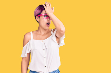 Young beautiful woman with pink hair wearing casual clothes and glasses surprised with hand on head for mistake, remember error. forgot, bad memory concept.