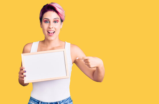Young beautiful woman with pink hair holding empty white chalkboard smiling happy pointing with hand and finger