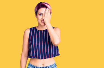 Young beautiful woman with pink hair wearing casual clothes covering one eye with hand, confident...