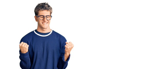 Young handsome man wearing casual clothes and glasses very happy and excited doing winner gesture with arms raised, smiling and screaming for success. celebration concept.