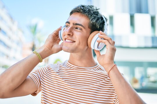 Young handsome caucasian man smiling happy listening to music using headphones walking at city.