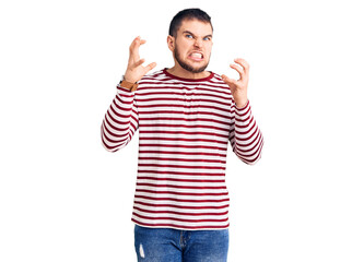 Young handsome man wearing striped sweater shouting frustrated with rage, hands trying to strangle, yelling mad